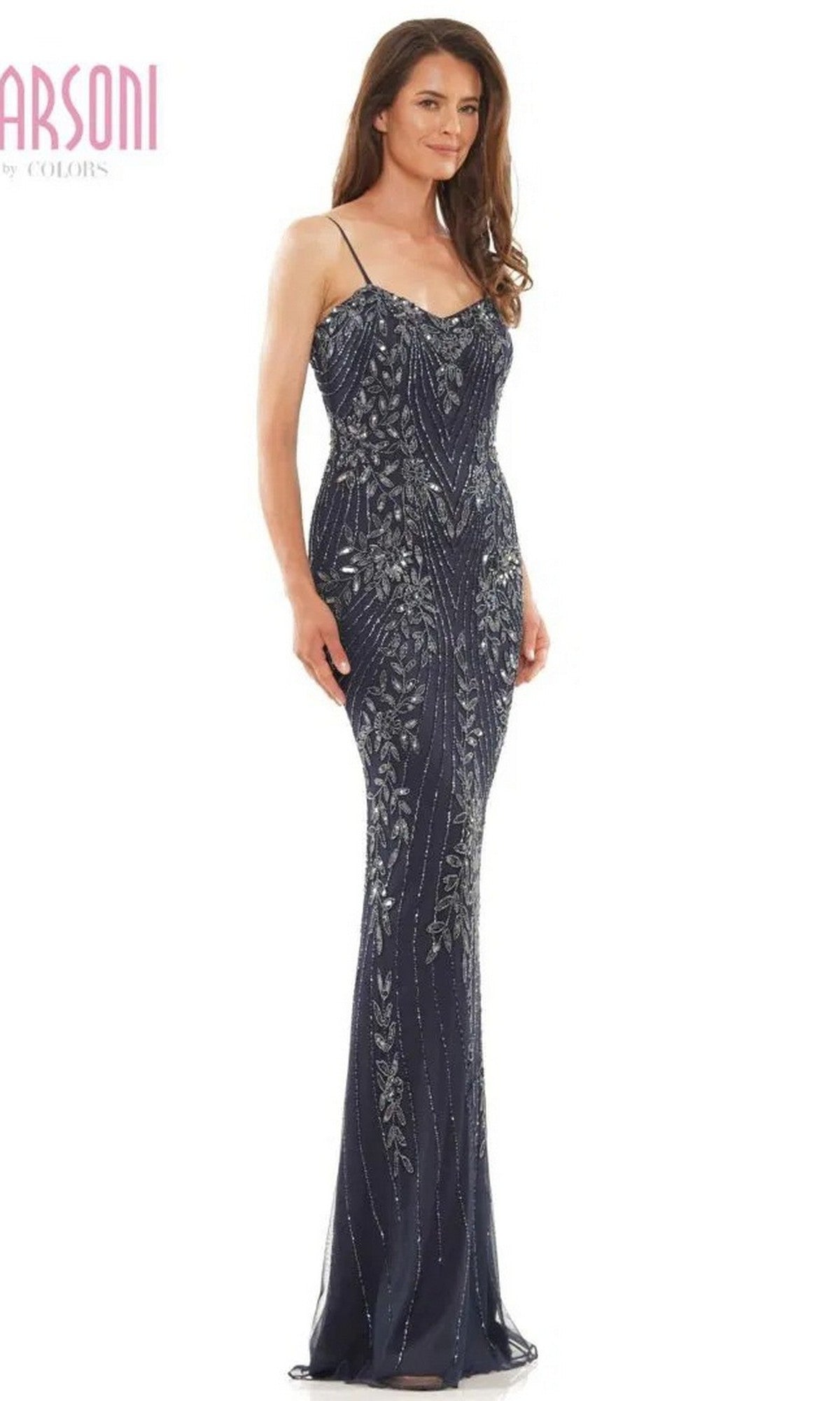 A woman models the Marsoni MV1201, a long, dark blue formal dress with thin straps, silver sequin patterns, intricate beading, and a floor-length skirt—perfect for an elegant occasion.
